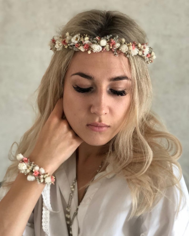May include: A white and pink floral crown with small white flowers and pink accents. The crown is worn on a person's head.
