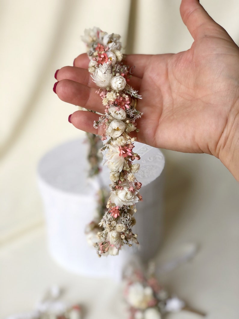 May include: A delicate floral crown made with dried flowers in shades of white and pink. The crown is made with small, delicate flowers and is perfect for a special occasion.