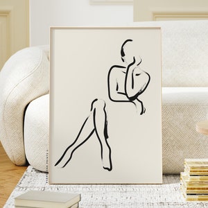 Pu&ograve; includere: Un disegno in bianco e nero di una persona in una posa contemplativa, stampato su carta color crema e incorniciato in una cornice di legno chiaro.