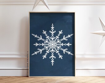Könnte beinhalten: Ein weißes Schneeflocken-Design auf dunkelblauem Hintergrund. Der Druck ist in einem goldenen Rahmen gerahmt und hängt an einer weißen Wand mit weißen Papiersternen, die von der Decke hängen.