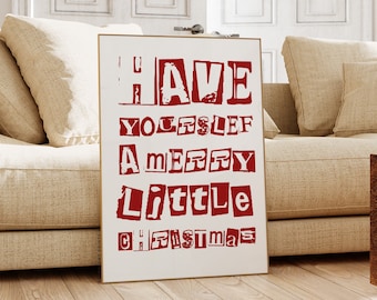 Può includere: Un poster bianco con testo rosso che recita "HAVE YOURSELF A MERRY LITTLE CHRISTMAS". Il poster è appoggiato a un divano beige in una stanza con pareti bianche e pavimento in legno.