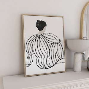 Puede incluir: Un dibujo en blanco y negro de una persona con un vestido, enmarcado en un marco dorado, colgado en una pared blanca sobre una repisa blanca.
