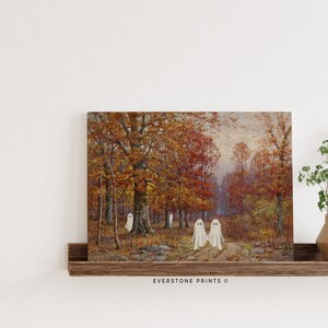 May include: A vintage painting of a forest scene with fall foliage in shades of red, orange, and yellow.  Three white ghosts are walking on a path in the woods.  The painting is framed and hanging on a wall.