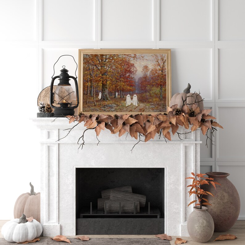 May include: A white fireplace mantel decorated with a fall garland of brown leaves and pine cones. A framed painting of a forest scene with white ghosts hangs above the fireplace. A white pumpkin sits on the floor in front of the fireplace.