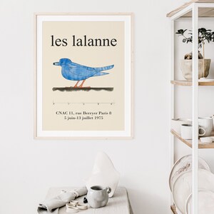 May include: A framed poster with a blue bird illustration and the text "les lalanne" in black. The poster also includes the text "CNAC 11, rue Berryer Paris 8 5 juin-13 juillet 1975".