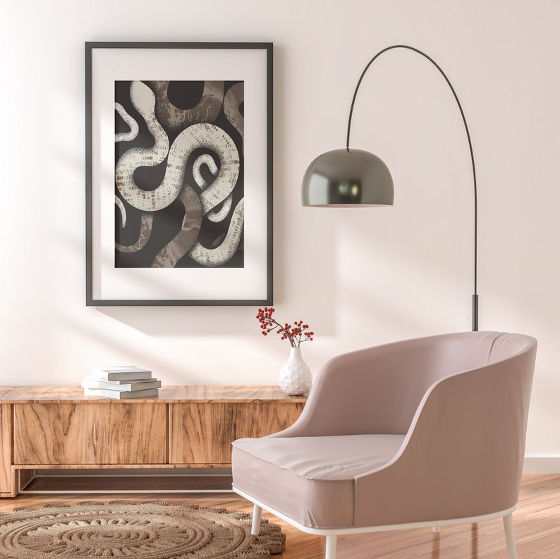 May include: A framed print of a black and white abstract snake design hangs on a white wall above a wooden console table. A pink armchair sits in front of the table with a small vase of red berries on the table.