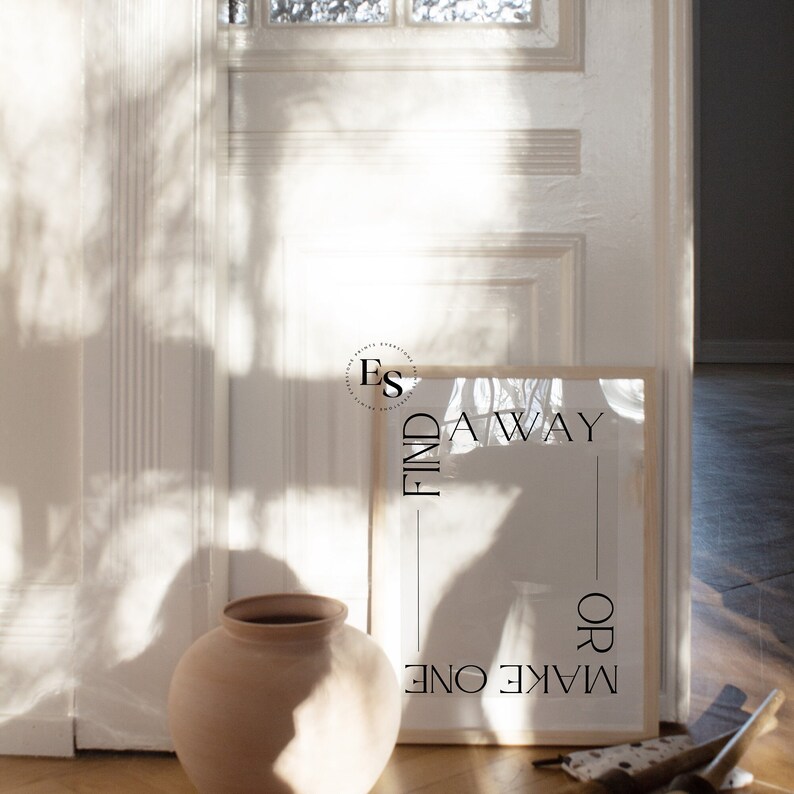 May include: A framed print with the text "FIND A WAY OR MAKE ONE" in a white frame on a wooden floor. The print is leaning against a white door with a shadow cast on the wall.