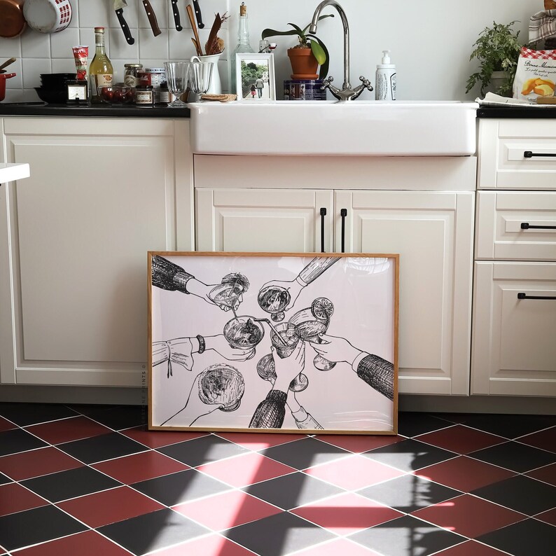 Op de afbeelding: Een zwart-witte illustratie van mensen die hun glazen heffen voor een toast. De illustratie is ingelijst in een licht houten lijst en hangt aan een witte muur.