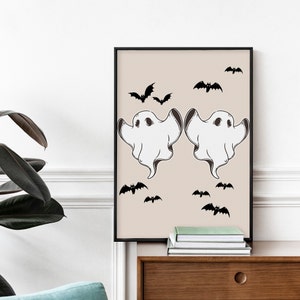May include: A printable Halloween art print featuring two white ghosts with black eyes and a black outline. The ghosts are flying against a beige background with black bats scattered around them.