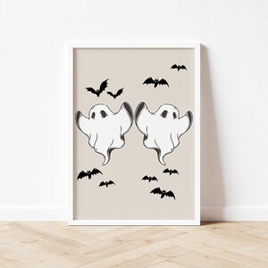May include: A printable wall art design featuring two white ghosts with black eyes and a beige background.  The ghosts are facing each other and have their arms raised.  There are several black bats scattered around the ghosts.