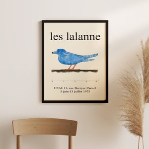 May include: A black framed poster with the text "les lalanne" in white. The poster features a blue bird with an orange beak and legs, standing on a black line. The text "CNAC 11, rue Berryer Paris 8 5 juin-13 juillet 1975" is at the bottom of the poster.