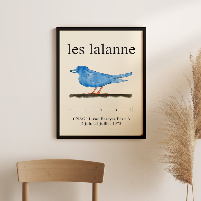 May include: A black framed poster with the text "les lalanne" in white. The poster features a blue bird with an orange beak and legs, standing on a black line. The text "CNAC 11, rue Berryer Paris 8 5 juin-13 juillet 1975" is at the bottom of the poster.