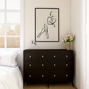Pu&ograve; includere: Un disegno in bianco e nero di una persona seduta con le gambe incrociate. Il disegno &egrave; incorniciato e appeso a una parete bianca sopra una cassettiera marrone scuro con sei cassetti.