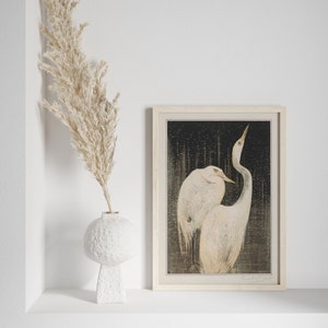 Op de afbeelding: Een ingelijste print van een zwart-witte illustratie van twee witte reigers die samen staan. De reigers bevinden zich in een bosrijke omgeving met een donkere achtergrond. De print is in een licht houten lijst.