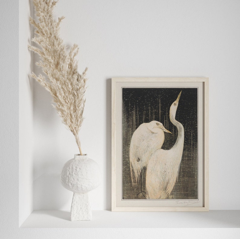 Op de afbeelding: Een ingelijste print van een zwart-witte illustratie van twee witte reigers die samen staan. De reigers bevinden zich in een bosrijke omgeving met een donkere achtergrond. De print is in een licht houten lijst.