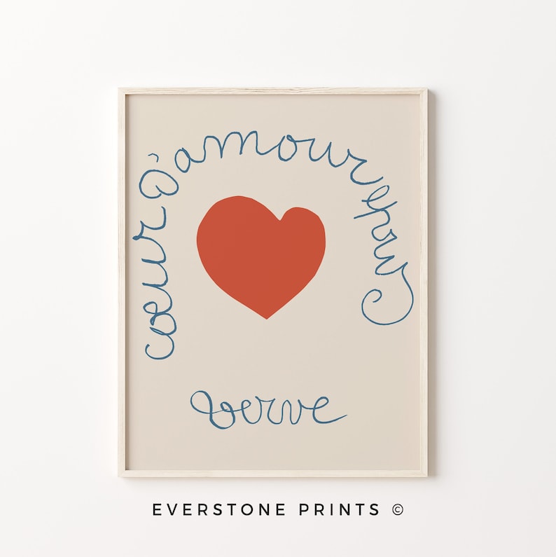 May include: A beige printable art print with a red heart and blue cursive text that reads "coeur d'amour" and "serve" in a circular shape around the heart. The print is framed in a light wood frame.