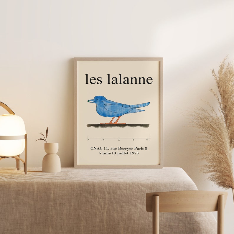 May include: A framed poster with the text "les lalanne" in black lettering. A blue bird with orange feet is depicted on a white background. The poster also includes the text "CNAC 11, rue Berryer Paris 8 5 juin-13 juillet 1975".