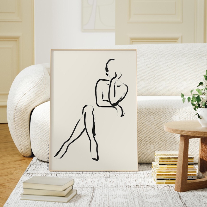 Pu&ograve; includere: Un disegno in bianco e nero di una persona in una posa contemplativa, stampato su carta color crema e incorniciato in una cornice di legno chiaro.