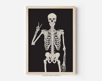 May include: A black and white illustration of a skeleton giving the peace sign. The skeleton is standing against a black background and is framed in a light wood frame. The text "EVERSTONE PRINTS ©" is at the bottom of the frame.