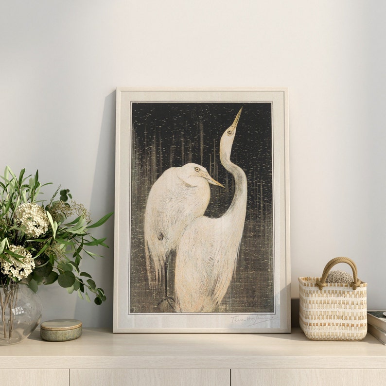 Op de afbeelding: Een ingelijste print van een zwart-witte illustratie van twee witte reigers met lange nek en snavel. De reigers staan op een donkere achtergrond met een textuurpatroon.