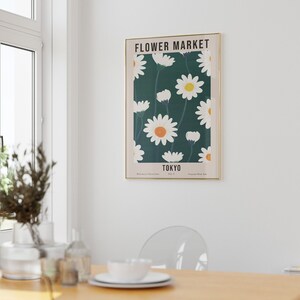 May include: A framed poster with a green background and white daisies with yellow centers. The poster says "FLOWER MARKET" and "TOKYO" in a white sans-serif font.
