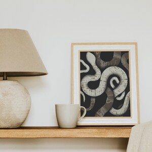 May include: A framed print of a black and white illustration of snakes intertwined. The snakes are a light gray color and have a textured pattern.