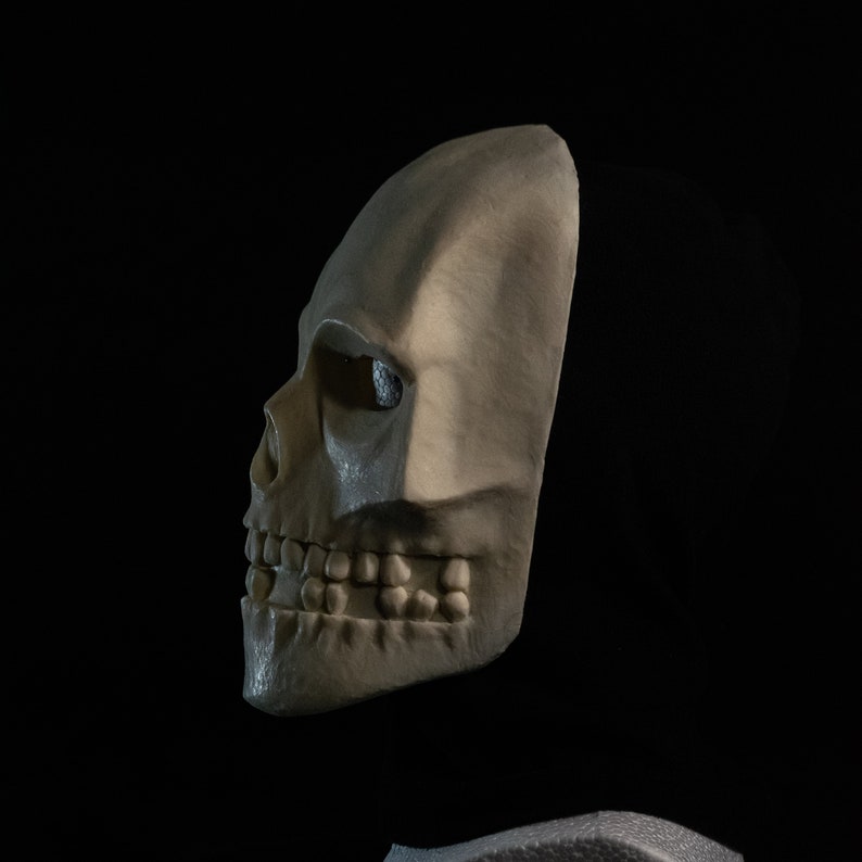 May include: A white skull mask with a detailed design, including teeth and eye sockets. The mask is made of a smooth, pliable material and is designed to fit over the head.