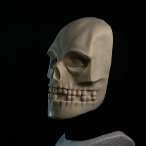 May include: A white skull mask with a detailed, realistic design. The mask has a closed mouth with teeth and a single eye socket.