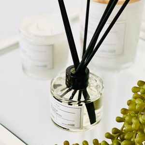 May include: A clear glass diffuser bottle with black reeds and a white label that reads "Diffuser - Lemon & Sandalwood". The bottle is sitting on a white surface with a green succulent plant.