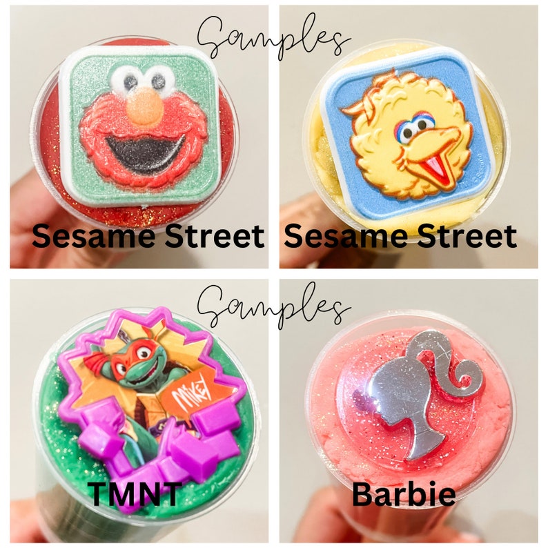 K&ouml;nnte beinhalten: Vier durchsichtige Plastikbecher mit buntem Schleim gef&uuml;llt. Jeder Becher hat einen anderen Charakter-Topper: Elmo, Big Bird, Teenage Mutant Ninja Turtles und Barbie. Die Becher sind mit "Sesame Street", "Sesame Street", "TMNT" und "Barbie" beschriftet.