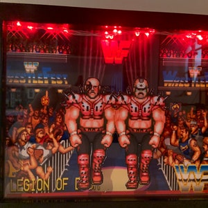 May include: A framed shadow box featuring a pixelated wrestling scene with two muscular figures in red and black attire. The background includes a crowd, the WWF logo, and the text "Wrestlefest". Red LED lights illuminate the scene.