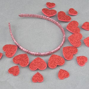May include: A red headband with a row of red glitter hearts attached to it. The hearts are arranged in a cascading pattern.