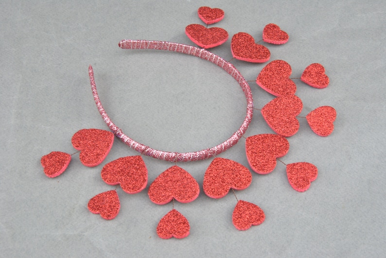 May include: A red headband with a row of red glitter hearts attached to it. The hearts are arranged in a cascading pattern.