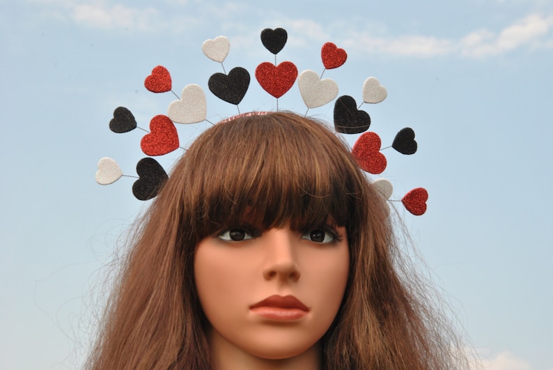 May include: A headband with a row of red, white, and black felt hearts. The hearts are attached to a silver wire headband.