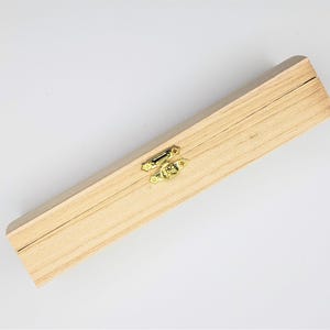 May include: A rectangular wooden box with a light finish. The box has a hinged lid and a gold-coloured clasp. The box is closed and appears to be empty. The box is made of wood and has a natural grain.