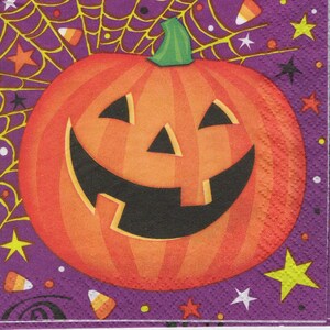 May include: A Halloween-themed napkin with a smiling jack-o'-lantern in orange and black. The purple background has a spider web, stars, and candy corn. The napkin is square.