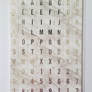 May include: Chipboard letter stickers with a marble design. The package includes 96 pieces with letters, numbers, and symbols. The text on the package reads "Chipboard Letter Stickers" and "Photo Safe".
