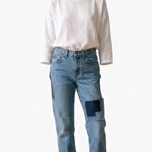 Puede incluir: Un atuendo informal con una camisa blanca de manga larga y vaqueros azul claro. Los vaqueros tienen un detalle de parche en una rodilla y est&aacute;n doblados en los tobillos. La camisa tiene un cuello redondo.