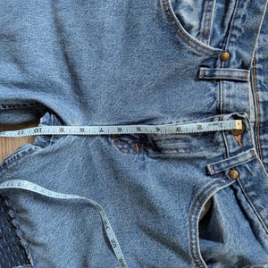 Puede incluir: Vaqueros de mezclilla azul claro con una cinta m&eacute;trica que muestra la medida de la cintura. Los vaqueros tienen un parche de tela azul oscuro en la pierna izquierda. La cinta m&eacute;trica muestra una medida de cintura de aproximadamente 25 cm.