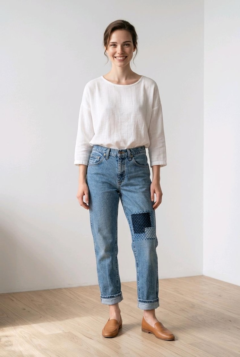 Puede incluir: Una persona viste una camisa blanca de manga larga y vaqueros azul claro con un parche en la rodilla. Tambi&eacute;n lleva mocasines de cuero marr&oacute;n. El atuendo es informal y c&oacute;modo.