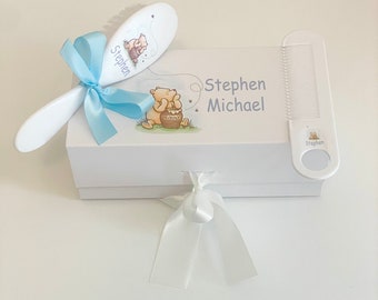May include: A white gift box with a blue ribbon and a Winnie the Pooh themed baby brush and comb set. The box is personalized with the name "Stephen Michael".