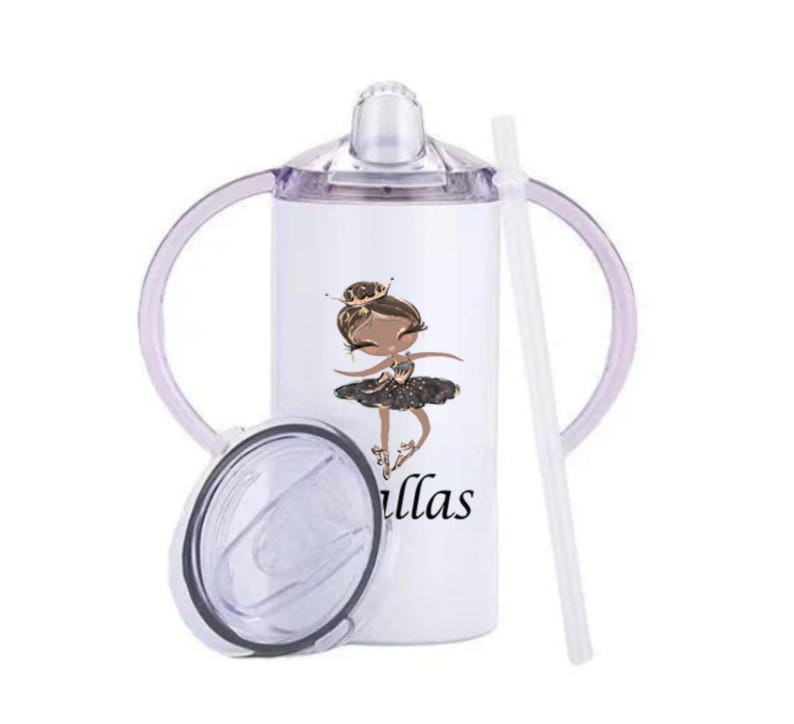 Op de afbeelding: Witte drinkbeker met een ballerina-afbeelding en de naam "Dallas" in zwart schrift. De beker heeft een doorzichtig deksel, een wit rietje en paarse handvatten. Ontworpen voor kinderen.