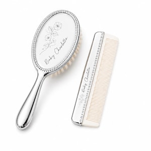 May include: A silver-toned baby hairbrush and comb set. The oval brush features a floral design and the name "Baby Charlotte". The comb and brush have a decorative border. The brush has soft bristles.