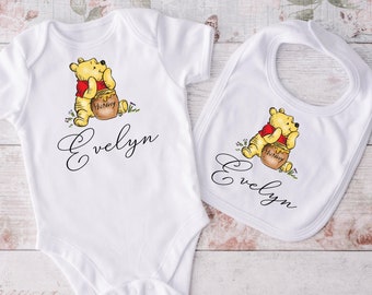 May include: White baby bodysuit and bib with Winnie the Pooh holding a honey pot. Both items feature the name "Evelyn" in cursive.