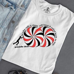 May include: White t-shirt with a black and red graphic of a person rolling a stone. The graphic is surrounded by the text "He who rolls a stone will have it rolled back on him" and "Proverbs 26:27".