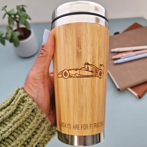 May include: A bamboo travel mug with a stainless steel lid and bottom. The mug has a laser-engraved image of a Formula 1 race car and the text "Sundays are for F1 racing".