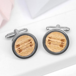 May include: A pair of silver cufflinks with a wooden inlay featuring a design of three arrows. The arrows are engraved into the wood and point to the right.
