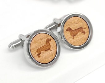 May include: A pair of silver cufflinks with a wood inlay featuring a dachshund silhouette.