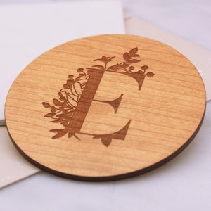May include: A wooden coaster with a floral design and the letter "E" engraved in the center.