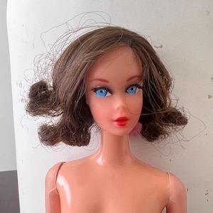 May include: A vintage doll with brown hair and blue eyes. The doll is wearing no clothing and has a light pink blush on her cheeks.